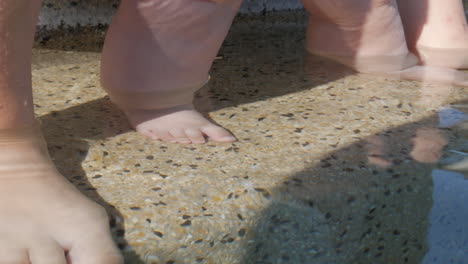 feet of a mother and her baby in clear pool water at summer