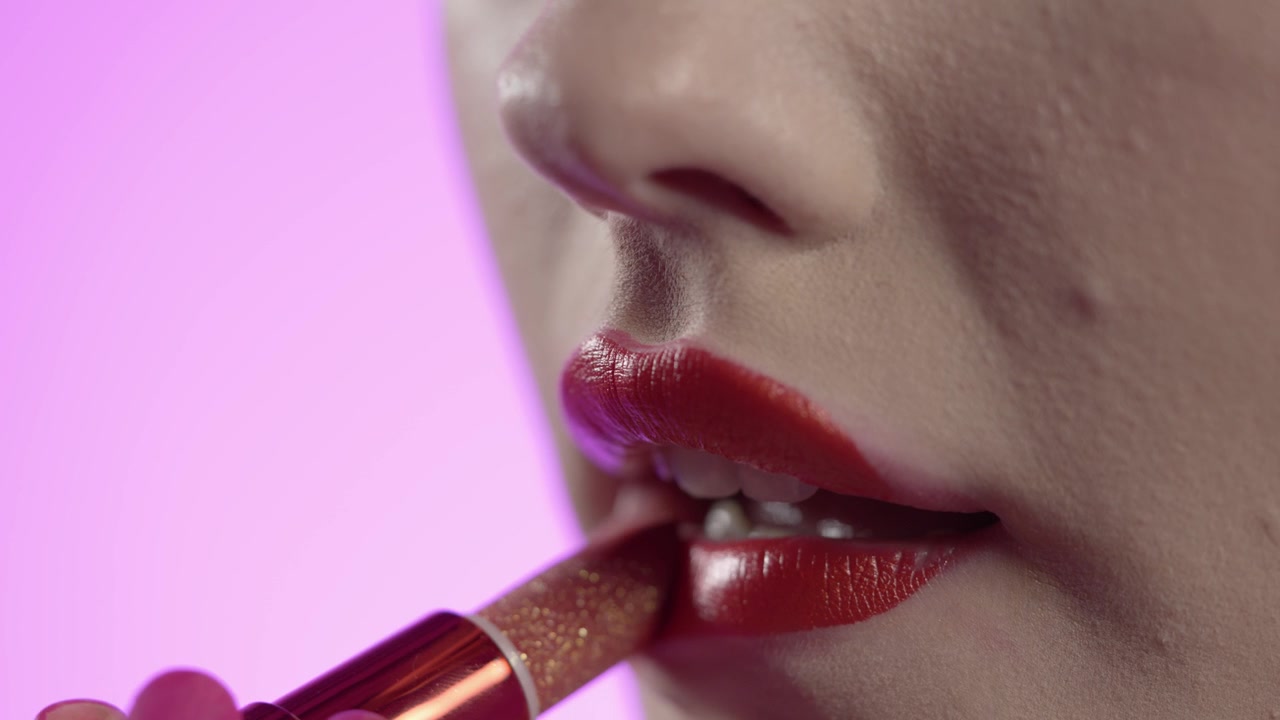 female applying lipstick on to red lips, pink background, make-up tutorial