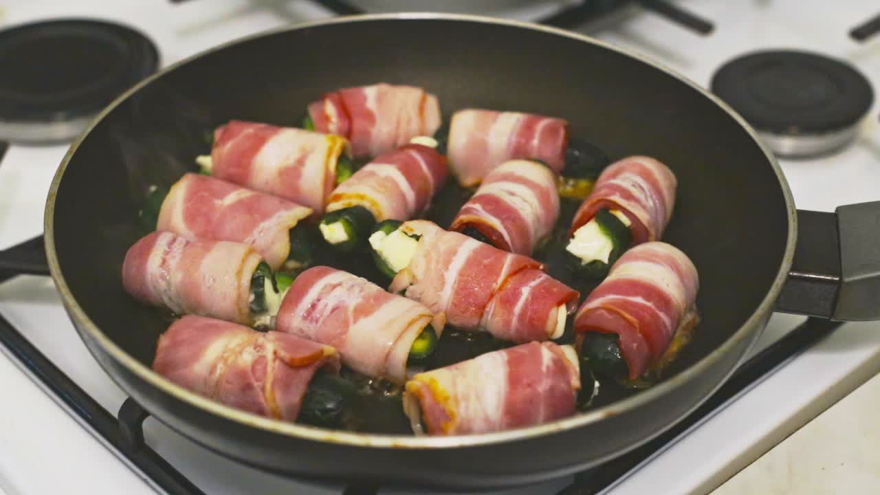 Jalapeno pepper stuffed with mozzarella, wrapped in bacon slowly frying on a pan