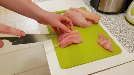 caucasian woman cooking and cutting up raw chicken breast meat