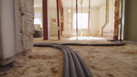 low angle shot of following electric cables running on the floor on a construction site, entering a room with huge windows