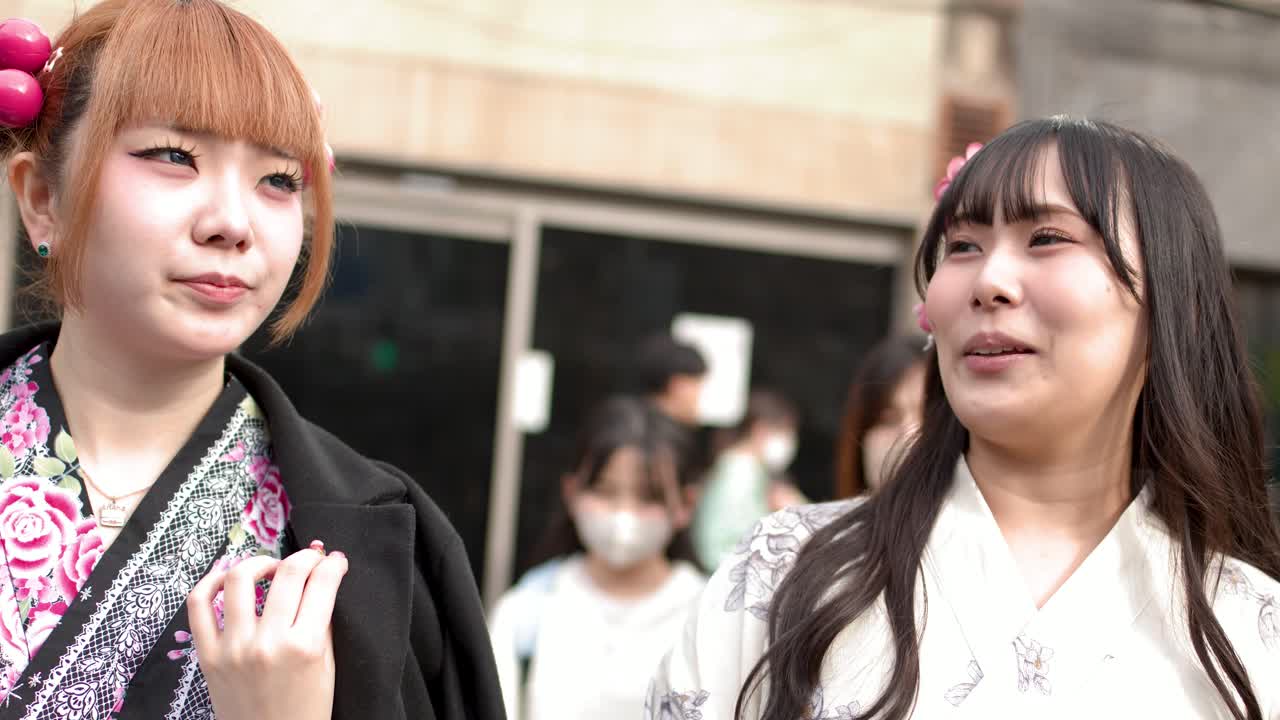 伝統的な着物と現代的なコートを着用した2人のアジア人女性が、東京の街中を歩きながら会話しています。