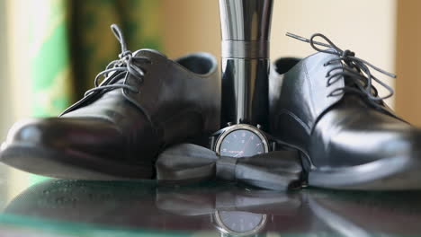 black shoes, a black watch, and a bottle of perfume with the black bow tie on the table for the groom