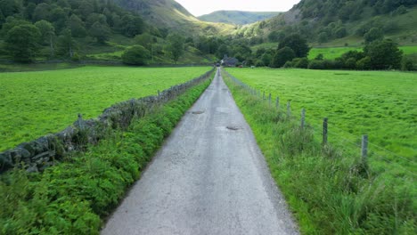 Moving-slowly-down-rural-lane-in-shaded-green-valley-towards-distant-farmhouse-and-sunlit-mountains-on-summer-day