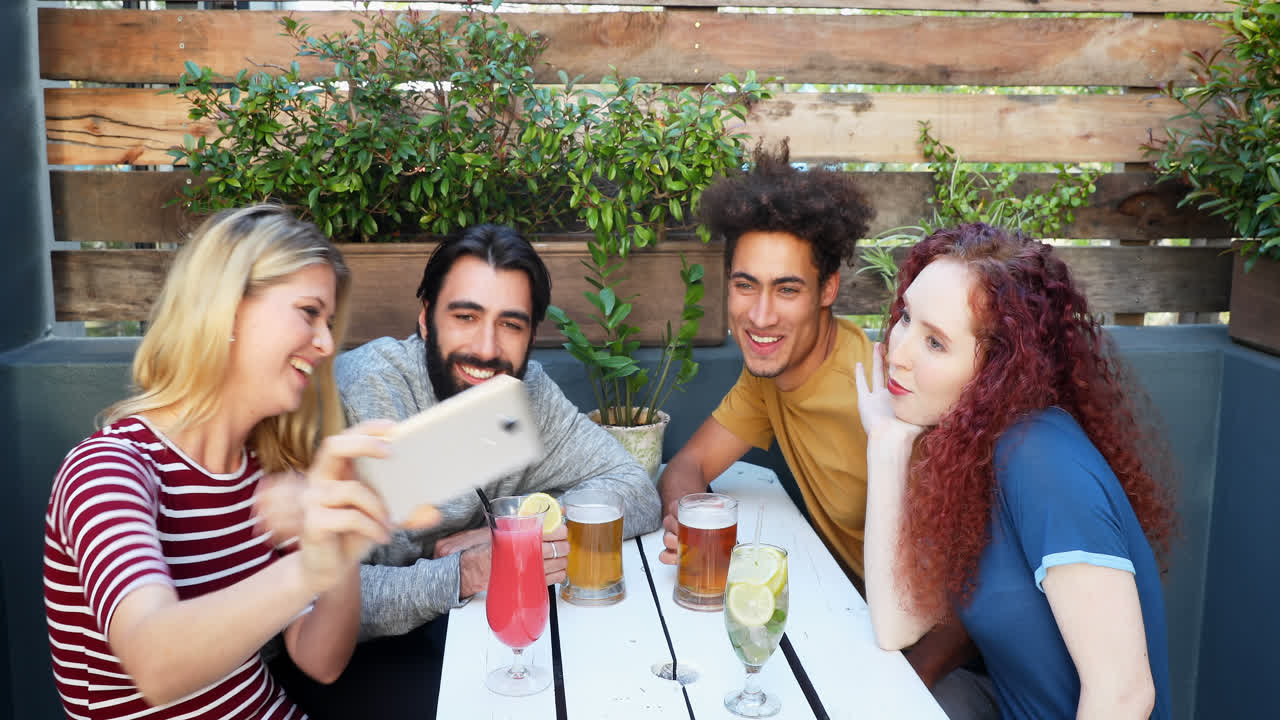 amigos tomando selfies con el teléfono móvil mientras toman bebidas en el bar 4k