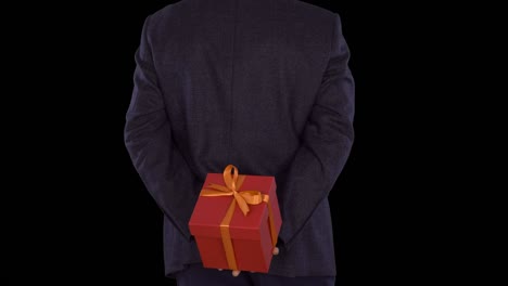 a man in a business suit is holding a red gift box behind his back. caucasian man shifts from foot to foot. businessman gives a gift. close up locked down shot. alpha channel chroma key. back view.