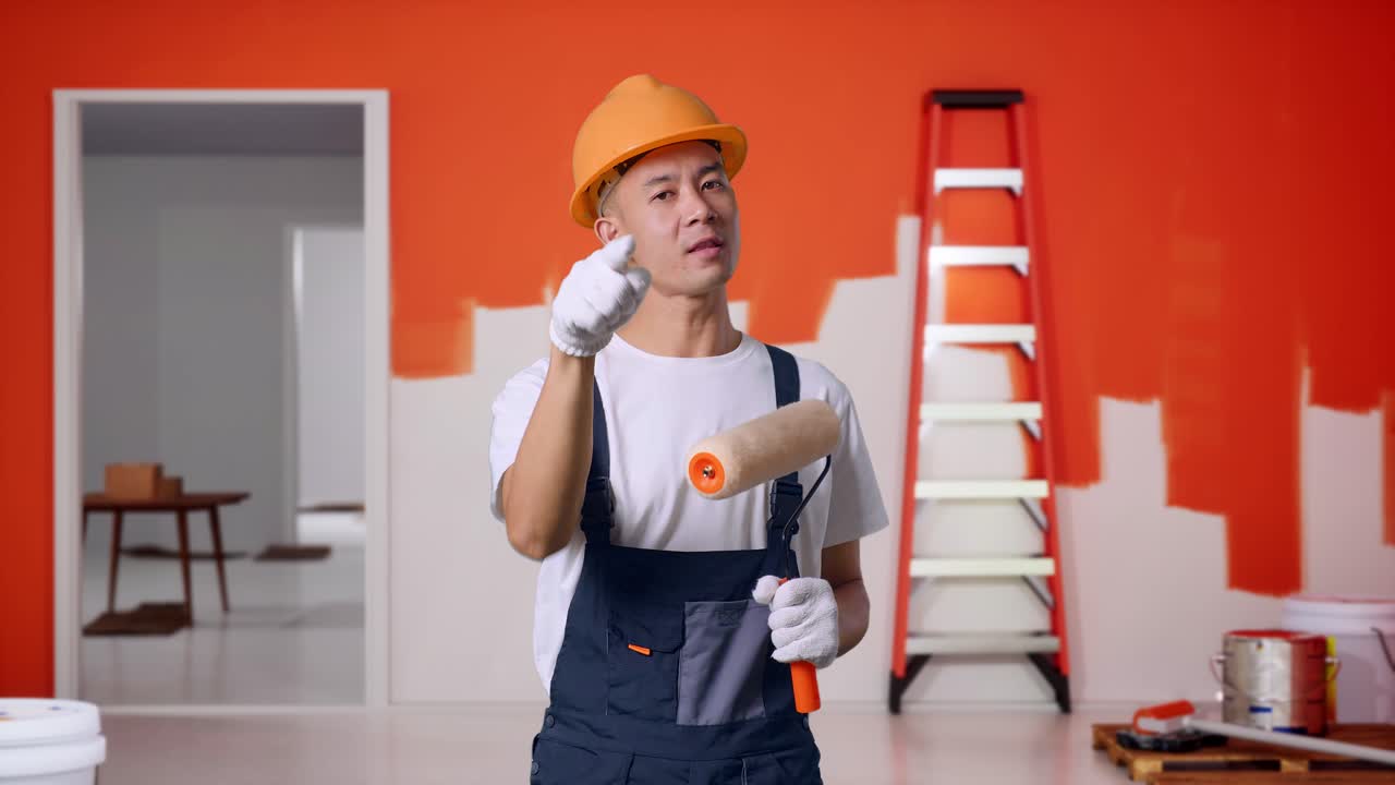 Asian Man Painter Wearing Safety Helmet Shouting To Camera While Standing With Painting Wall In Room