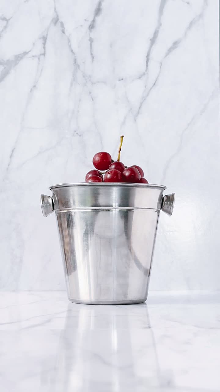 uvas rojas en un cubo de plata en una superficie de mármol