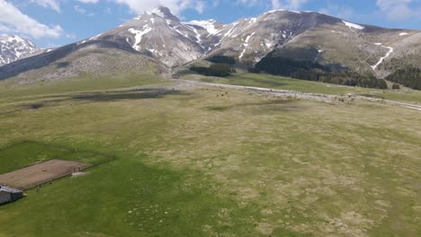 Wide-angle-drone-shot-scene-of-an-old-Sheppards-shelter-in-a-grassland-valley-surrounded-by-the-Gran-Sasso-mountain-range-in-the-rural-countryside-of-Abruzzo-in-Italy