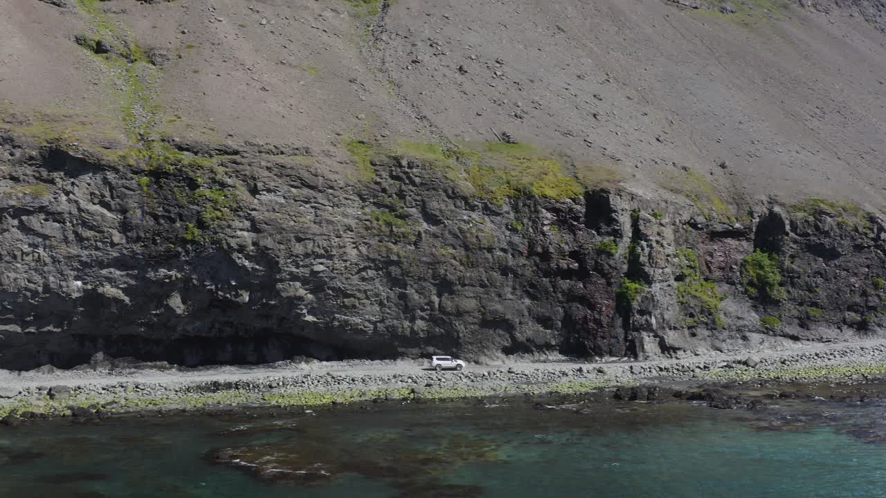아이슬란드 웨스트피요르드의 스발보가베구르 도로의 절벽 아래에서 운전하는 차량