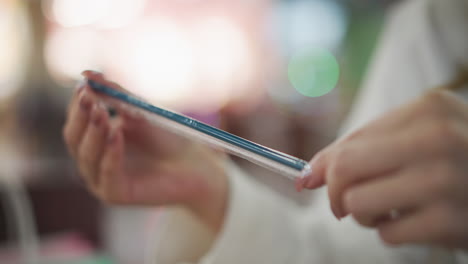 close-up of hands carefully removing a black straw from its protective sleeve in a modern indoor setting, with a softly blurred background featuring warm bokeh lights