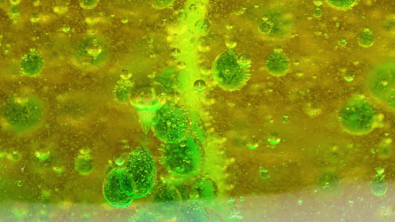 Green bubbles rise and interact dynamically within a vibrant yellow liquid, creating a mesmerizing visual effect.