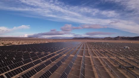 aerial drone footage of solar panel field in joshua tree national park on a sunny day with rainbow in the background, slow horizontal movement