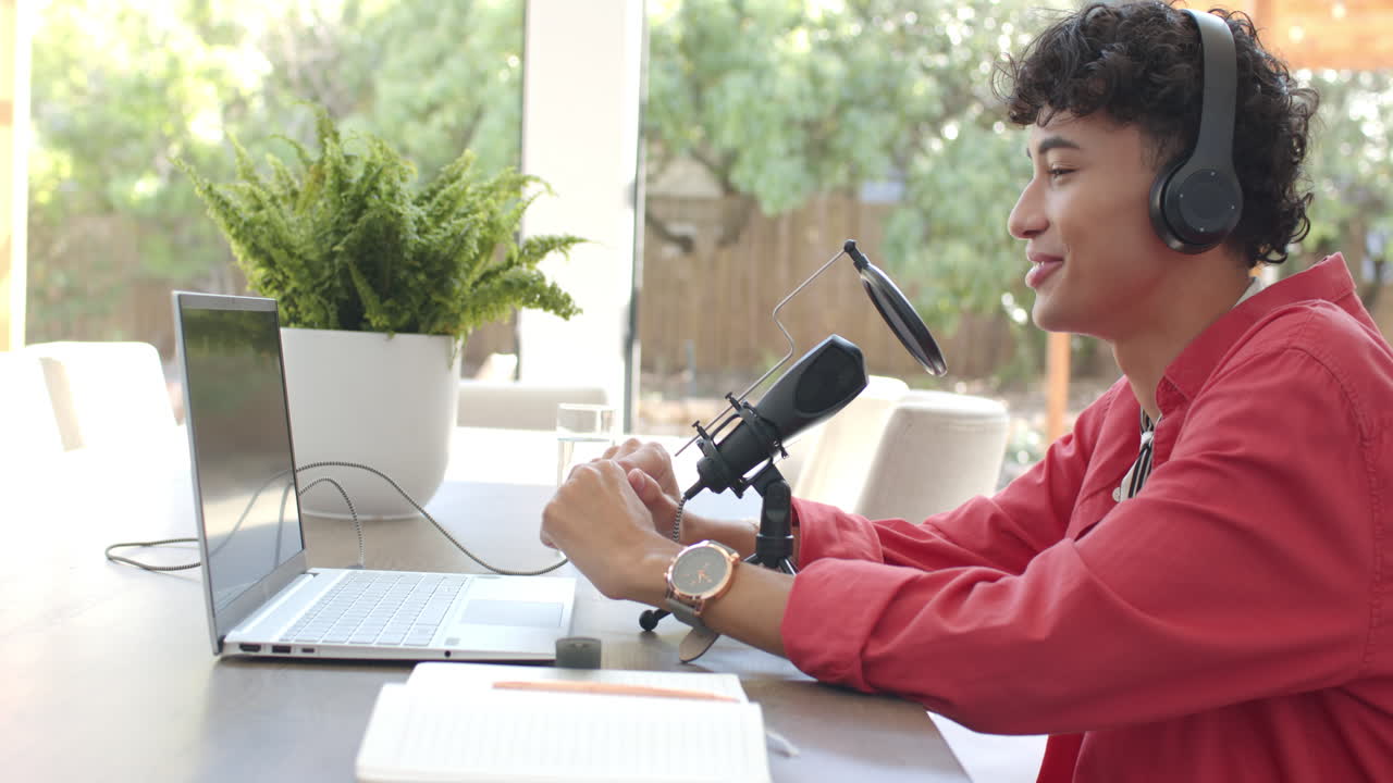 Recording podcast, teenage boy with headphones speaking into microphone at home office