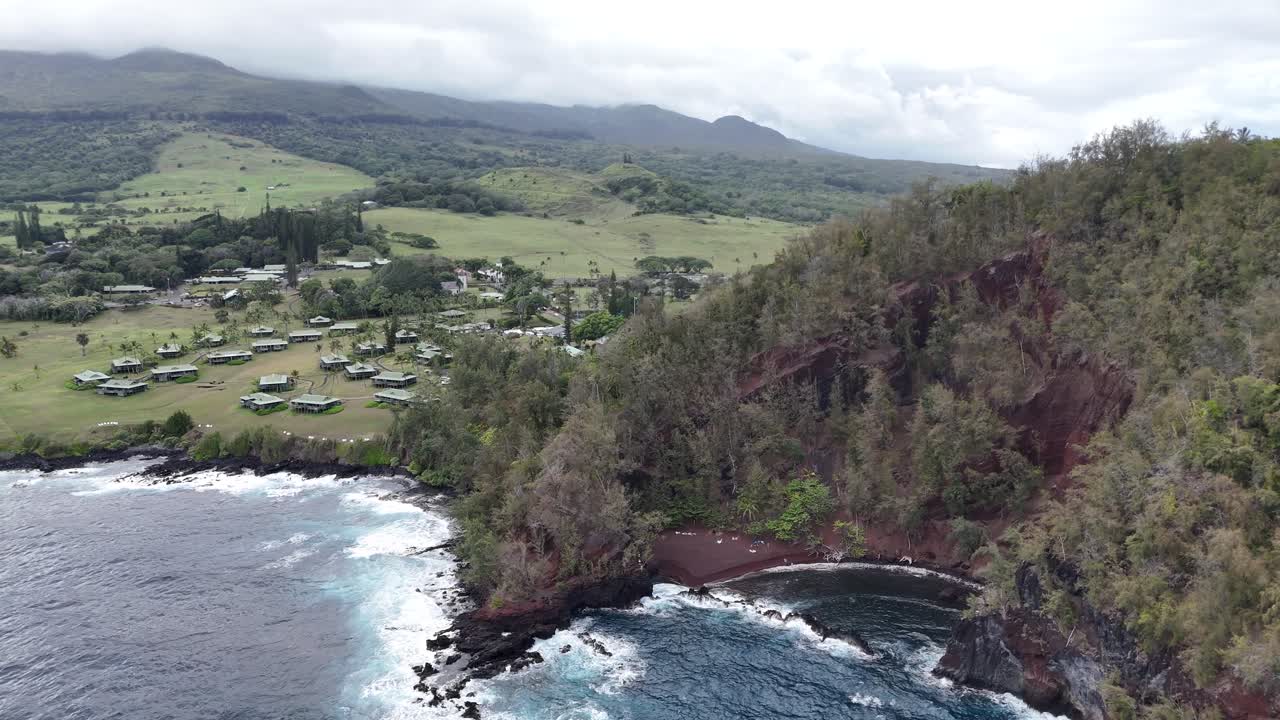 Drone approaching Hana, Maui, Hawaii showing the beach, coastal village, and lush mountains. Tropical paradise island vibes