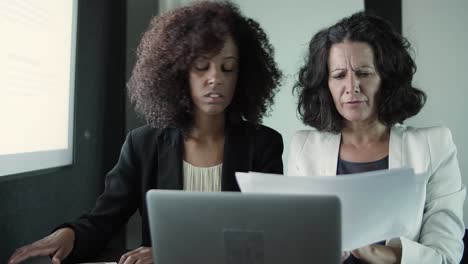 two content businesswomen sitting together and reading reports