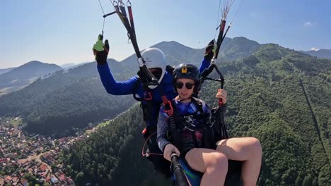 A-woman-parachutist,-accompanied-by-a-trainer,-embarks-on-a-delightful-flight-over-the-mountains-and-the-city,-she-is-capturing-her-airborne-adventure-with-a-camera-as-she-soars-above-Brasov,-Romania