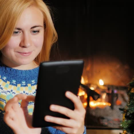 a young woman uses tablet near a christmas tree on a background of fire