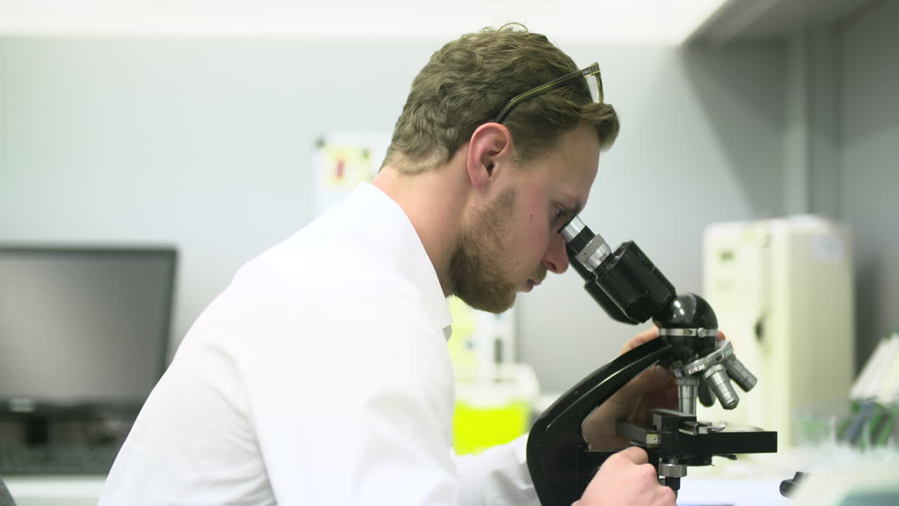 Scientist Examining Sample Through Microscope in Laboratory