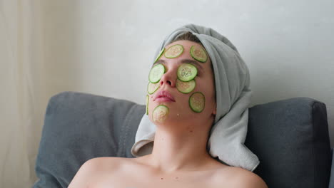 close-up of woman with hair wrapped in towel, cucumber slices placed on her face, relaxing in a peaceful self-care routine, she enjoys a soothing facial treatment while unwinding at home