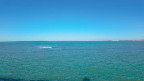 Vista-Tranquila-Y-Amplia-Del-Océano-Bajo-Un-Cielo-Azul-Claro,-Con-Suaves-Olas-Y-Un-Horizonte-Lejano,-Que-Evoca-Una-Sensación-De-Paz-Y-Vastedad.