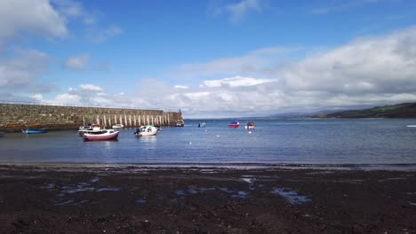 Trefor-harbour-at-ground-level-panning-left-to-right-with-view-of-harbour-wall-and-boats-at-low-tide-with-backdrop-of-blue-skies-on-a-summers-day-across-the-Irish-Sea-on-the-Llyn-Peninsula-in-Wales