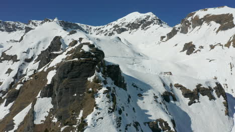 Aerial-of-snow-covered-rocky-mountain-top-with-ski-lifts-and-slope