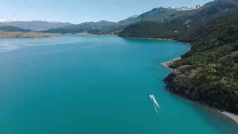 Vuelo-Aéreo-Sobre-El-Lago-Turquesa-Suave-General-Carrera-Con-Lancha-Rápida-Que-Pasa-Por-La-Costa