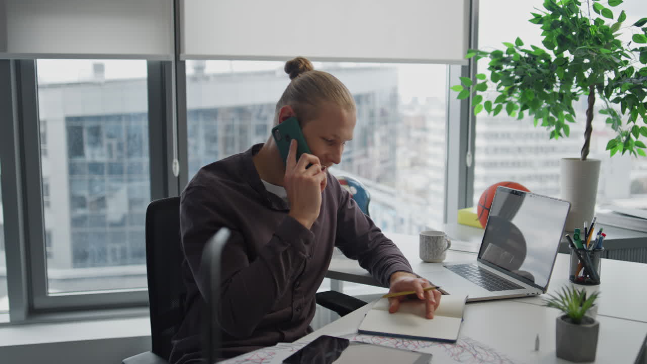 Travl forretningsmand taler i mobiltelefon indendørs tæt på. Positiv fyr skriver noter.
