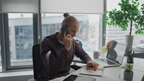 busy businessman speaking cellphone indoors close up. positive guy writing notes