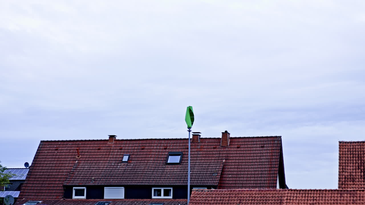 Colorful green object stands proudly on a pole above traditional rooftops in a quiet neighborhood during a cloudy day