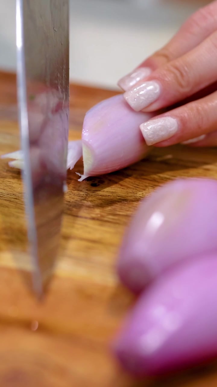 Close-up of hands slicing shallots on a wooden board with a sharp knife under bright lighting