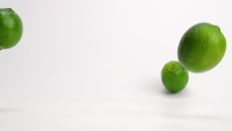 bright green whole limes bouncing in slow motion onto white table top