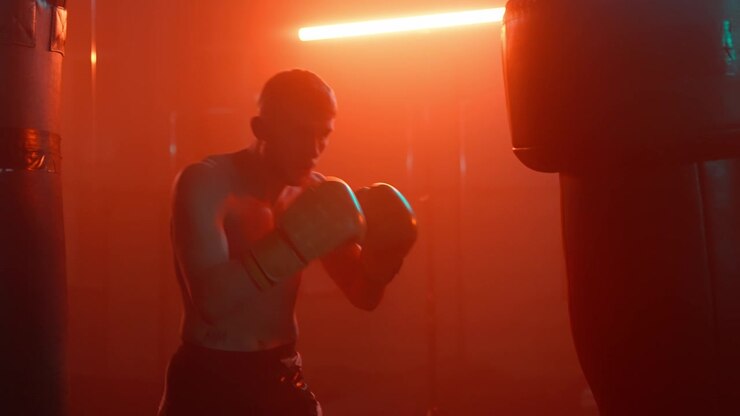 Boxeador entrenando con un saco de boxeo en un gimnasio iluminado en rojo