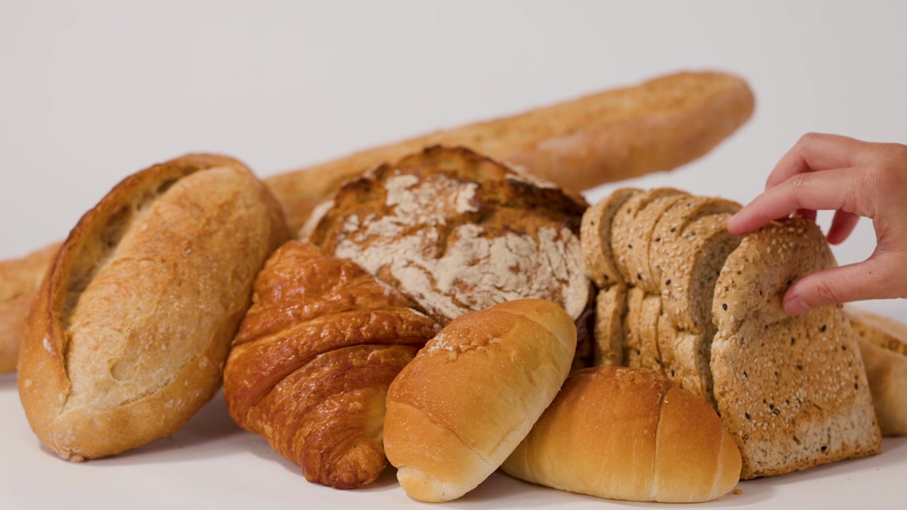 A hand selects sliced whole wheat bread from a variety of fresh bakery items.