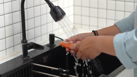 woman hands washing fresh orange carrots with running water over sink in kitchen, preparation to make smoothie vegetables