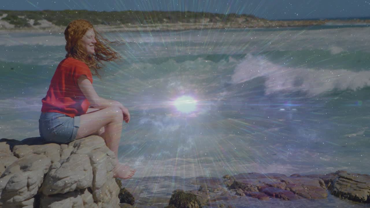 Woman settling on rocky outcrop initiating pulsing lens flare over ocean waves for travel marketing