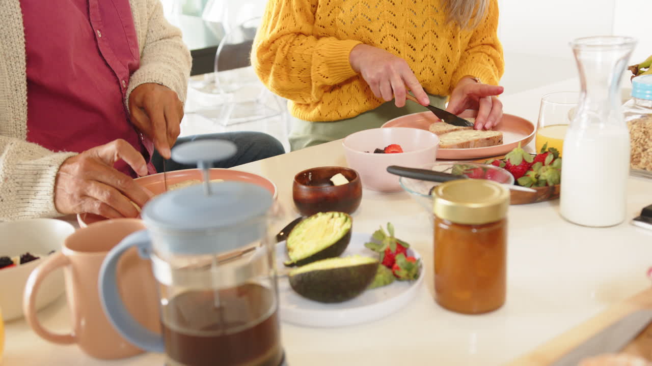 Preparing breakfast, woman spreading avocado on toast with ingredients on table, at home