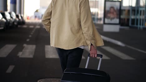 Close-up,-cropped-shot-of-married-man-with-the-black-baggage-walking-to-the-outside-airport-terminal-by-road.-Slow-motion.-Rare