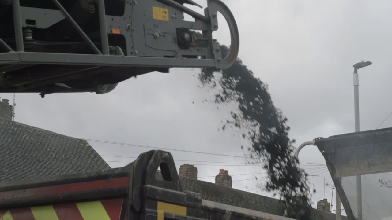 Heavy plant industrial milling machine loading asphalt onto truck medium shot