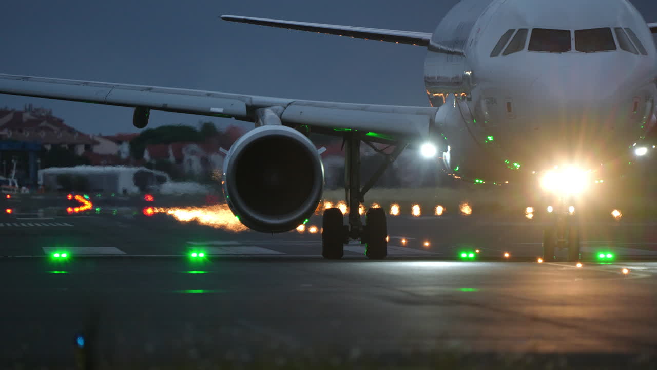 Front view of commercial airliner taxiing on runway with bright headlights in low light conditions