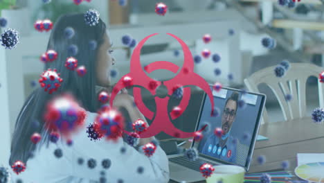 animation of covid 19 cells over biohazard sign and businesswoman on laptop video call