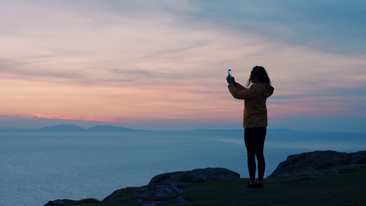 Woman taking photo of sunset over the ocean from a cliff