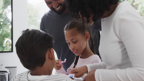 Happy-biracial-brother-and-sister-with-couple-brushing-teeth-in-sunny-bathroom,-slow-motion