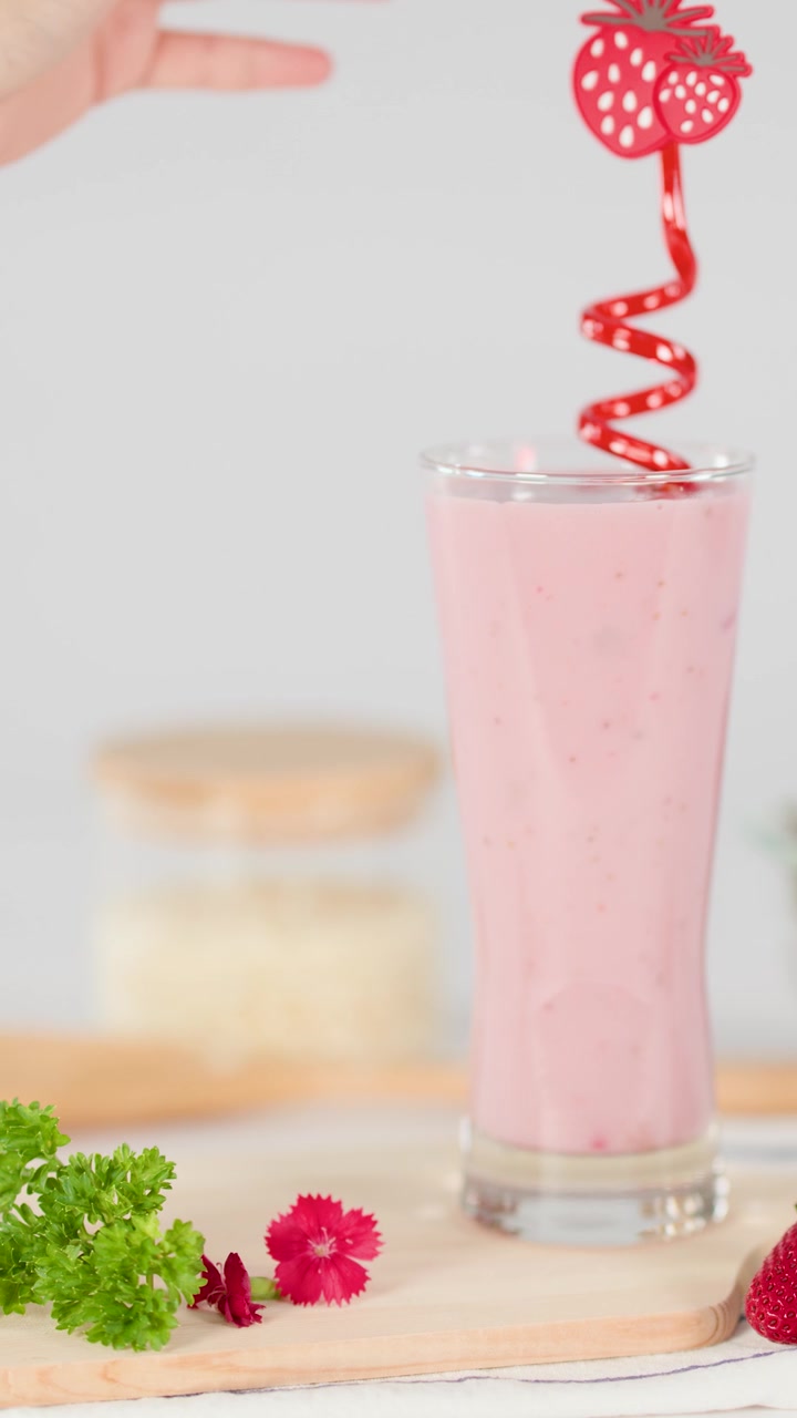 Mano che inserisce una cannuccia a spirale rossa in un cremoso milkshake alla fragola, sfondo luminoso, decorazione di frutta fresca.
