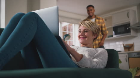 junges paar zu hause, das sich in der lounge entspannt und zusammen einen videoanruf mit dem laptop macht