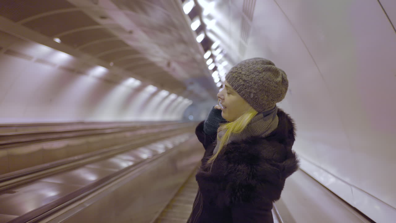 Woman riding a moving walkway in a brightly lit subway tunnel