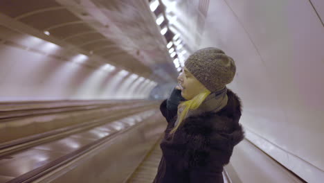 woman riding a moving walkway in a brightly lit subway tunnel
