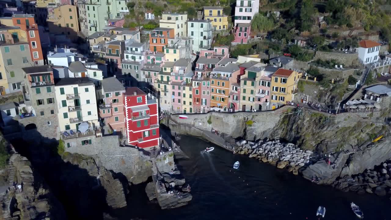Ville de Riomaggiore sur la côte italienne des Cinque Terre avec des bateaux et des personnes, plan aérien panoramique vers la droite