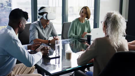 using vr headset, diverse team having meeting around glass table in office